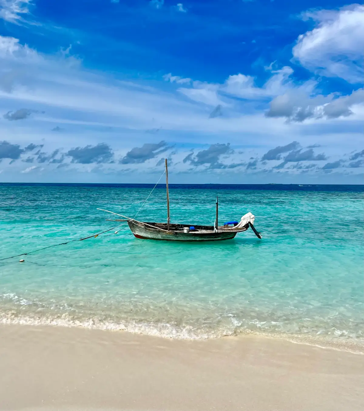 Traditionelles Holzboot ankert in türkisblauem Wasser vor weißem Sandstrand unter blauem Himmel mit Cumulus-Wolken